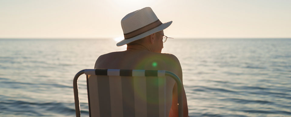 försäkring direkt sjuk försäkring, man i hatt sitter i en solstol vid havet i solnedgång